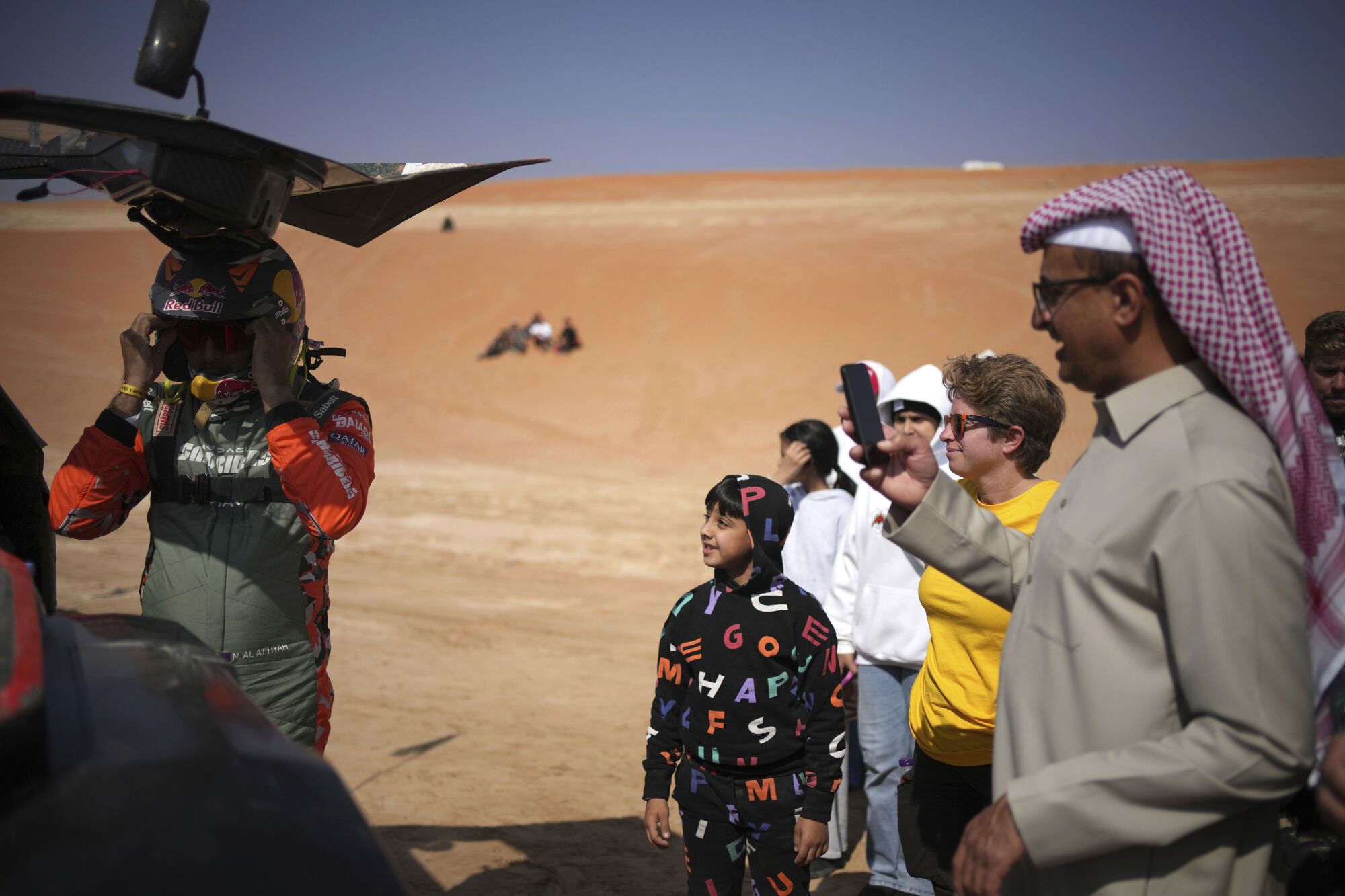 People watch driver Nasser Al-Attiya as he prepares at the start delayed due to fog during the eleventh stage of the Dakar Rally with start and finish in Shubaytah, Saudi Arabia, Thursday, Jan. 16, 2025. (AP Photo/Christophe Ena)